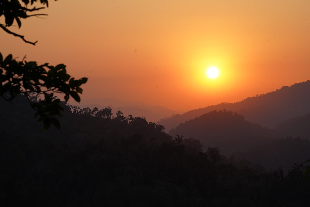 The sunset over some mountains and trees in the jungle in Laos.